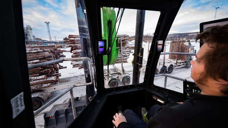 industriarbetare som sitter i en timmertruck och lastar av timmer från timmerlastbil