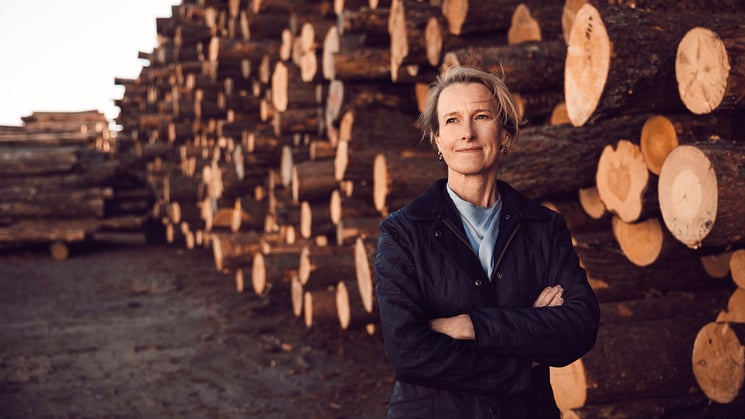 viveka beckeman på ett sågverk framför timmer