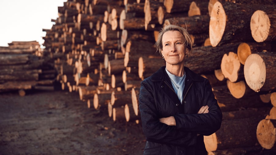 viveka beckeman på ett sågverk framför timmer