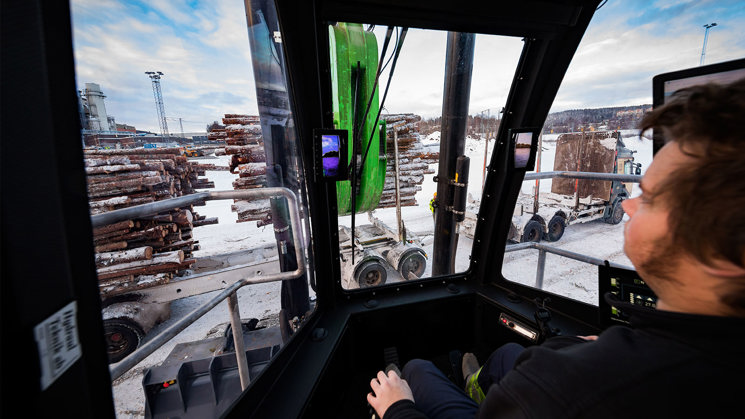 industriarbetare som sitter i en timmertruck och lastar av timmer från timmerlastbil