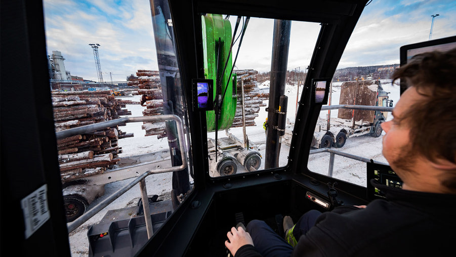 industriarbetare som sitter i en timmertruck och lastar av timmer från timmerlastbil